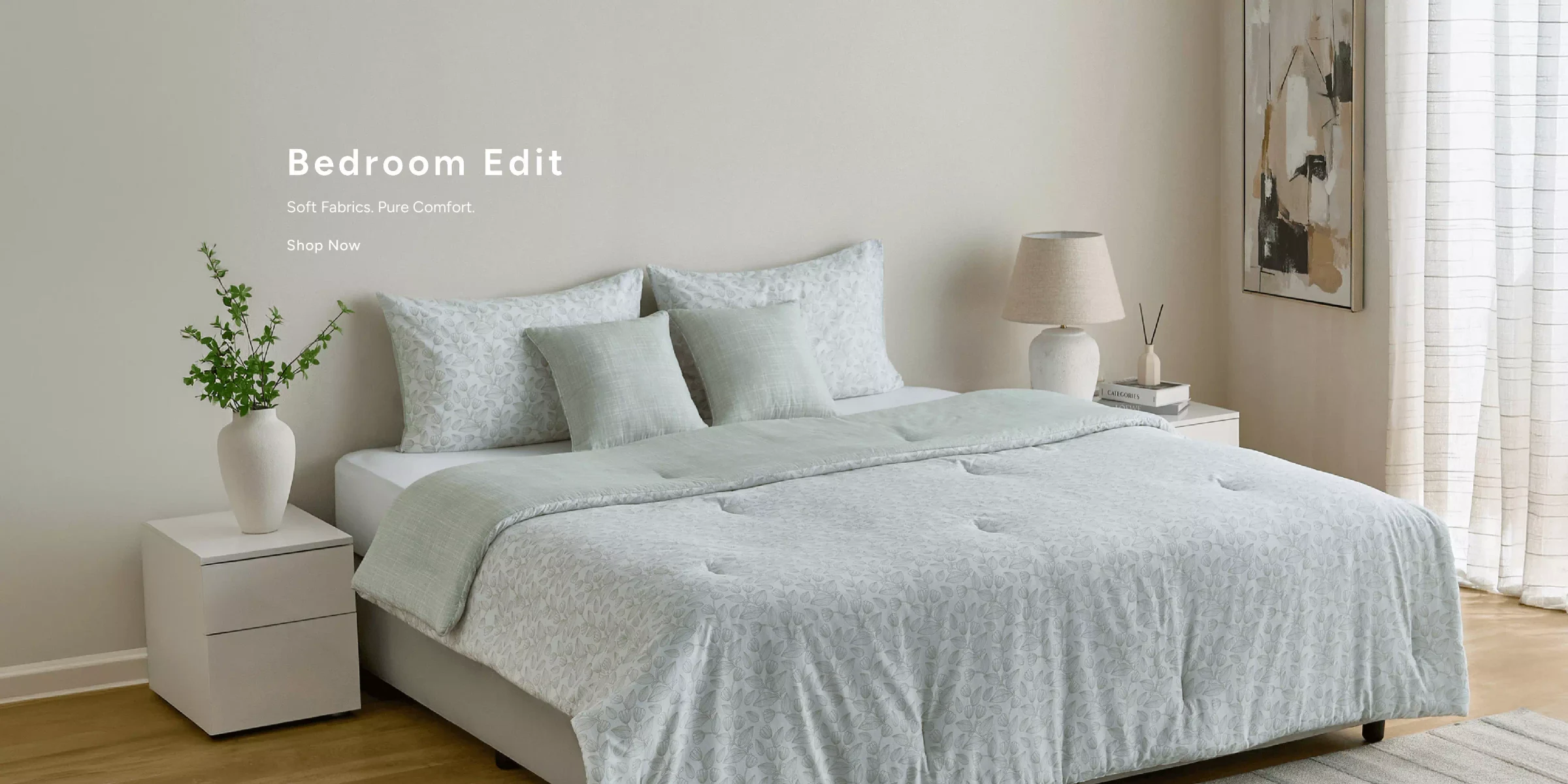 Bedroom Edit. Soft fabrics, pure comfort — sage quilted bedding, cushions and a bedside lamp in a calm bedroom. Shop home.