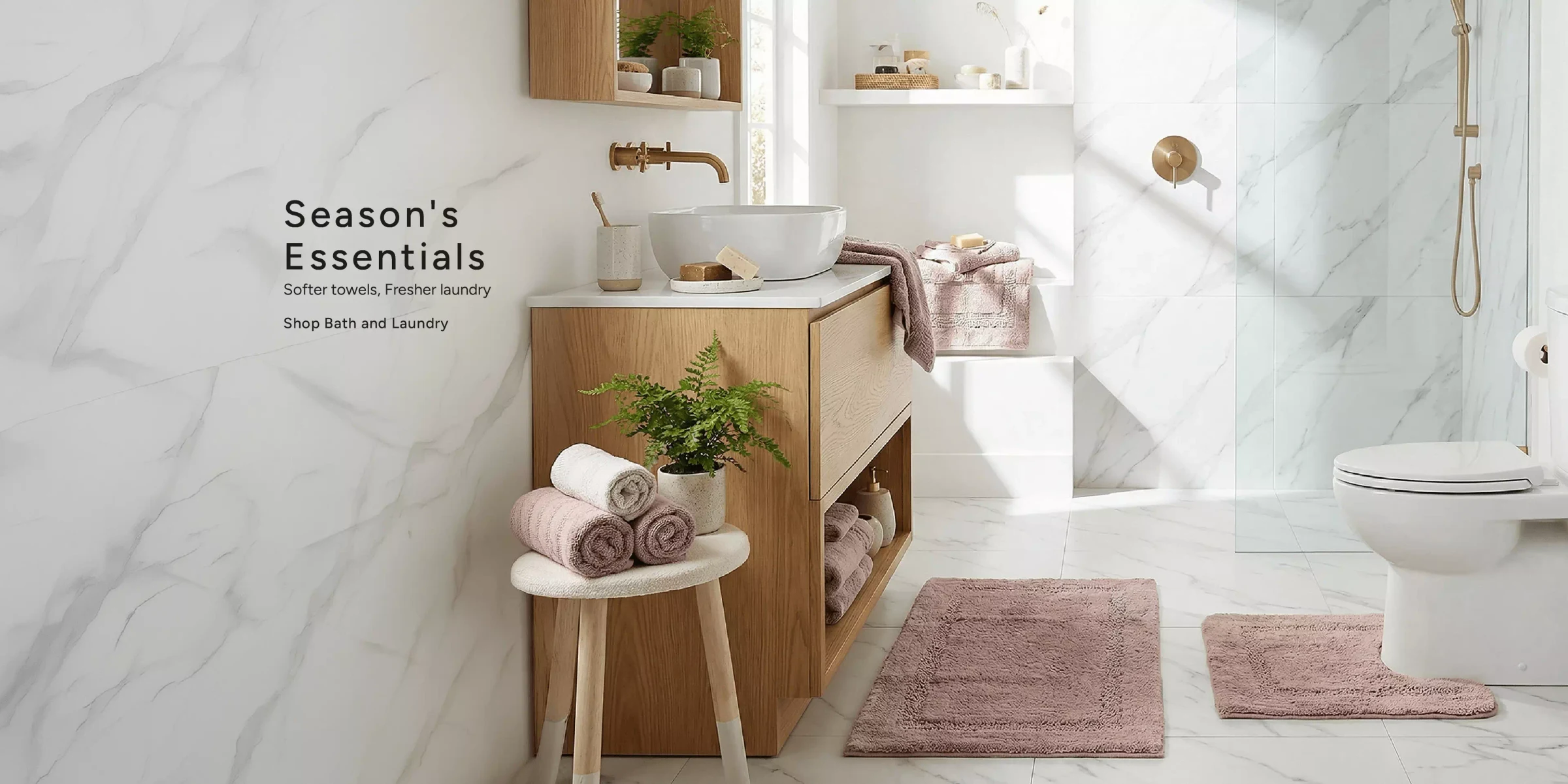 Season's Essentials. Softer towels, fresher laundry — blush bath mats, rolled towels and warm brass fittings in a marble bathroom. Shop bath and laundry.